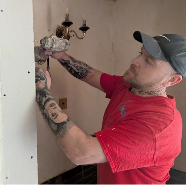 A plasterer with a drill, fitting boards to a wall