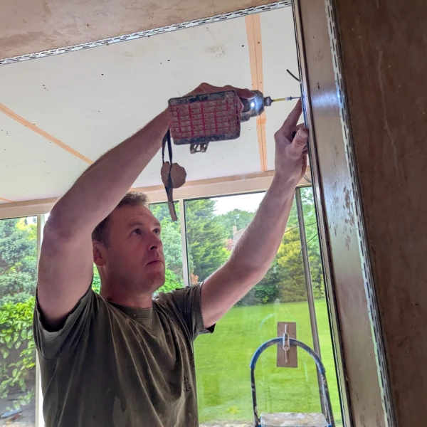 A workman uses a power screwdriver to put up metal trim on a wall corner